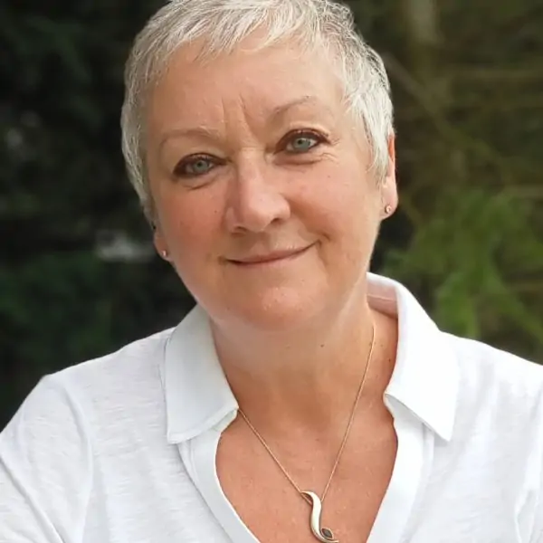 A white woman in her fifties is smiling to the camera. She has short, white hair and wears a white shirt.
