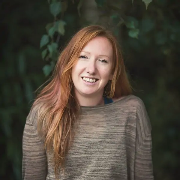 A white woman in her thirties is smiling to camera. She has ginger hair and is wearing. agreen long sleeve top.